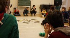 deux enfants, de dos, observent des objets sonores placés au centre d'un groupe d'élèves
